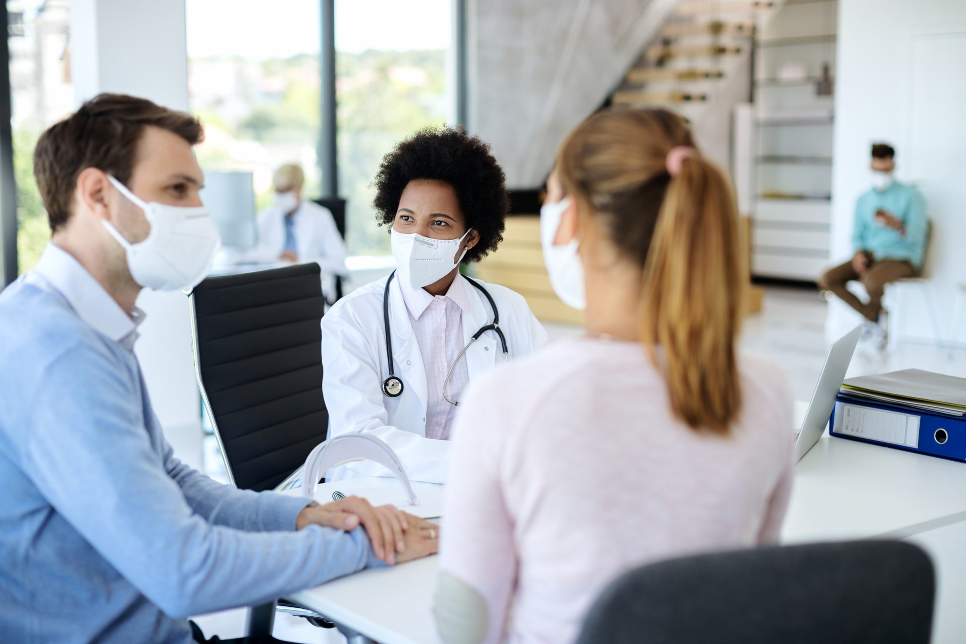 Smiling black doctor with face mask talking to a couple during m