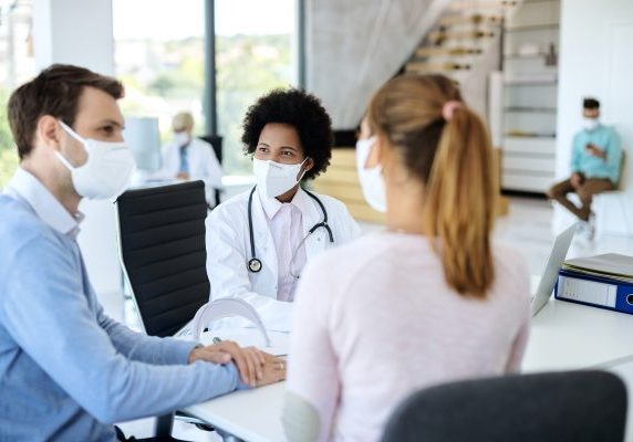 Smiling black doctor with face mask talking to a couple during m